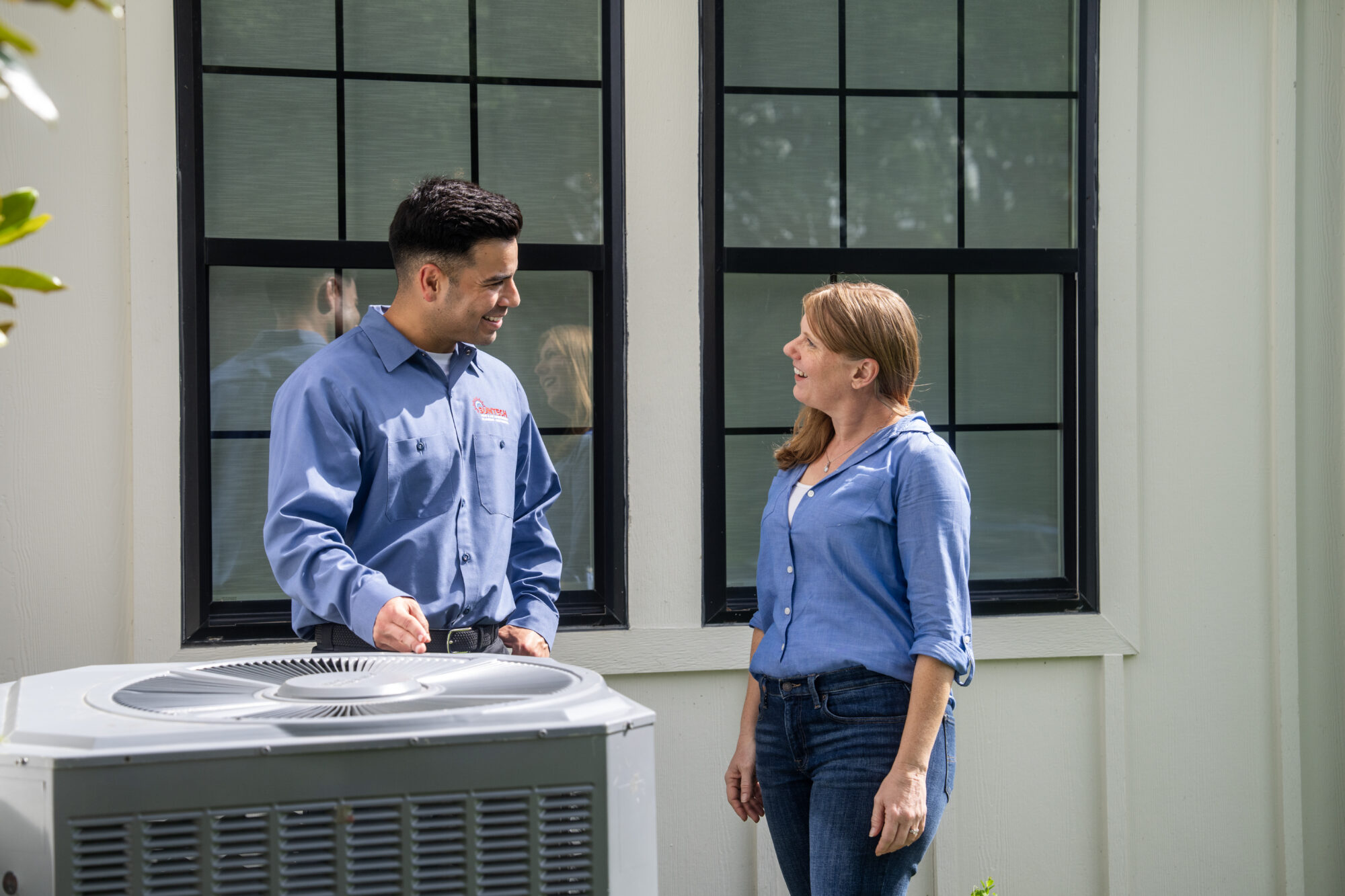 HVAC technician discussing an air conditioning unit with a homeowner outside their home